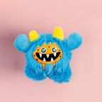 Blue fuzzy monster toy with yellow horns on a pink background