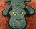 Green textured crocodile toy face close up on brown carpet