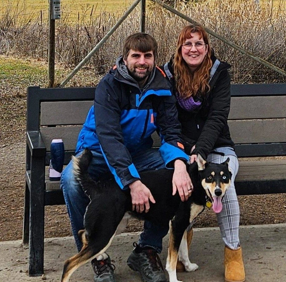 Two people sitting on a bench with a dog in an outdoor setting